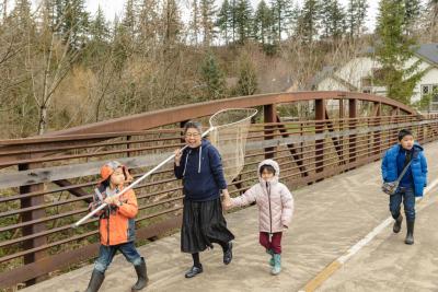 An older woman smiles as she carries a long dipnet toward the Sandy River with a group of kids. Photo by Marlee Boxler