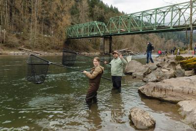 A couple smiles and gestures toward the camera as they dip for smelt in the Sandy River. Photo by Marlee Boxler