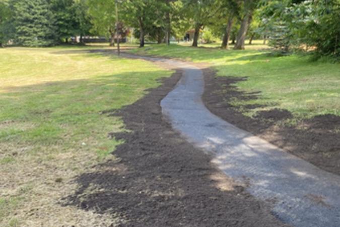 A newly paved path runs adjacent to large, leafy trees